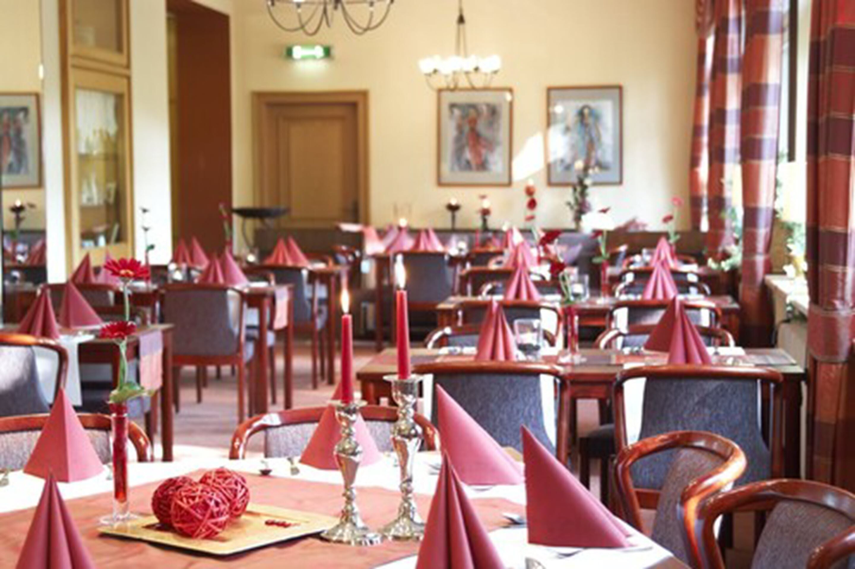 Un espace repas avec des tables décorées de serviettes rouges, de bougies et d’un centre de table ornemental.
