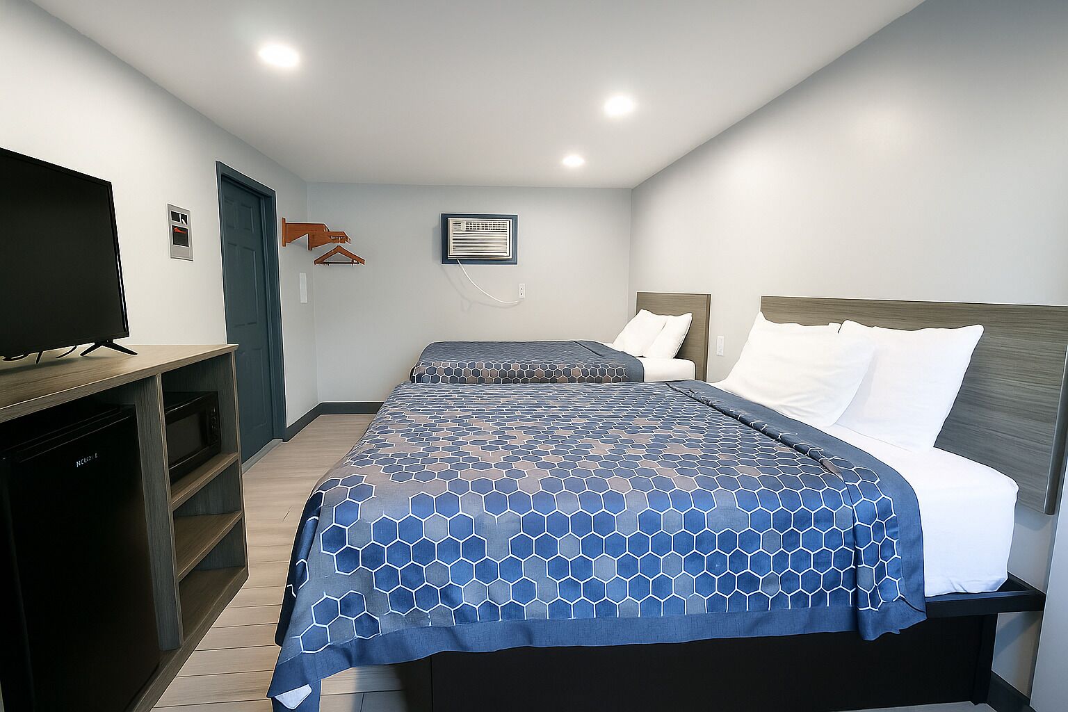 A hotel room with a large bed, a TV on a stand, and a desk with a computer.