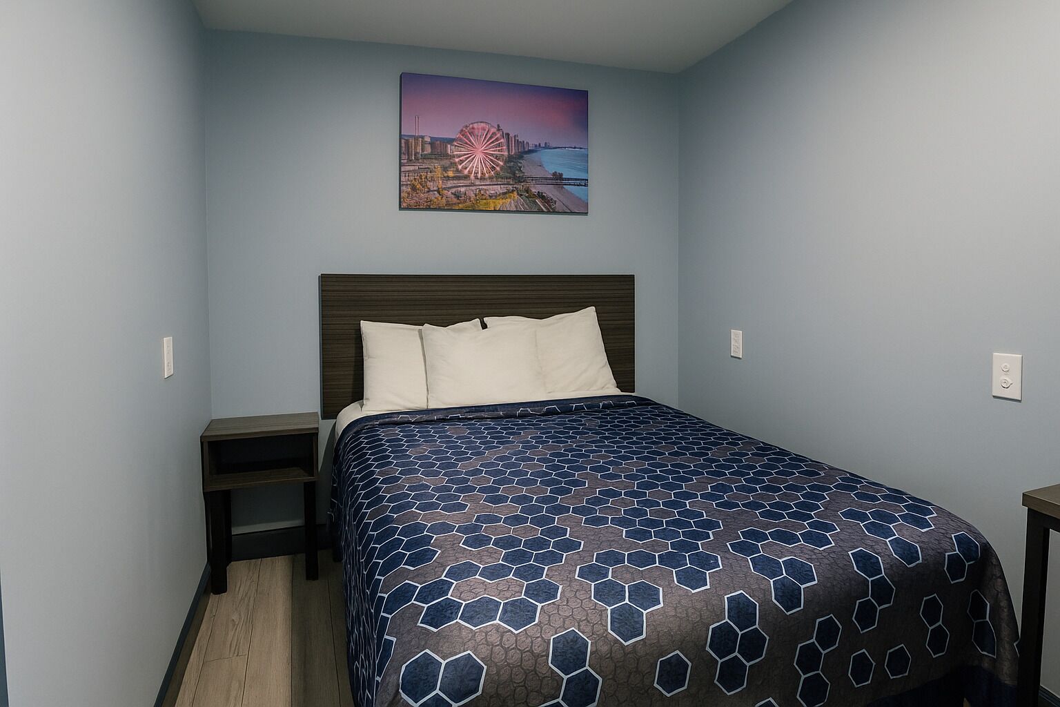 Un dormitorio con cama, mesita de noche, cabecera y un cuadro colgado en la pared.