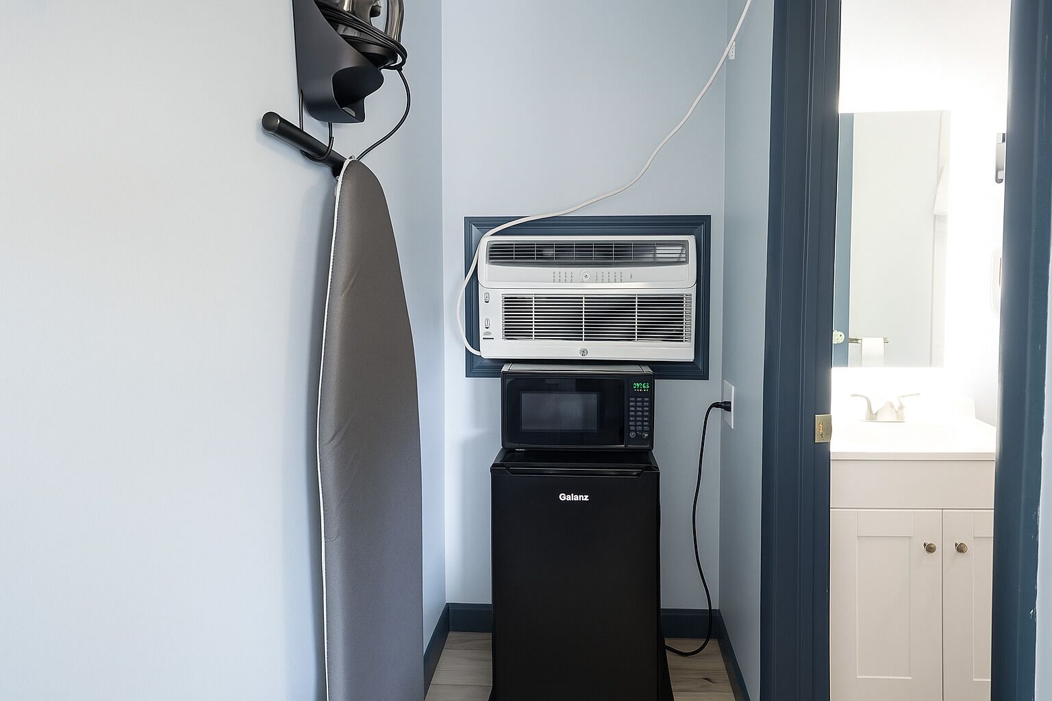 A compact kitchenette with a microwave and a wall-mounted air conditioner.