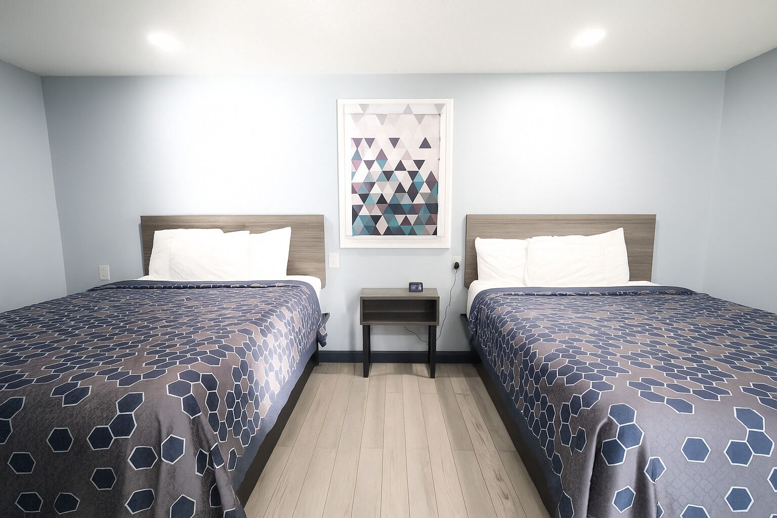 A hotel room with two beds, a small bedside table, and a geometric-patterned artwork on the wall.