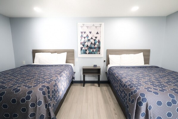Habitación de hotel con dos camas, una mesita de noche pequeña y una obra de arte con un diseño geométrico en la pared.