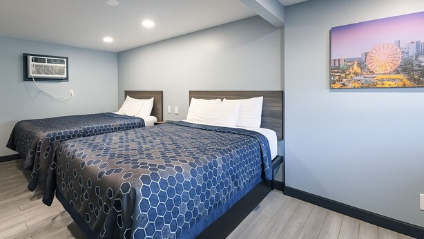 A hotel room with two beds, a cityscape painting, and a mounted air conditioner. - Hillsboro Inn & Suites (Hillsboro)