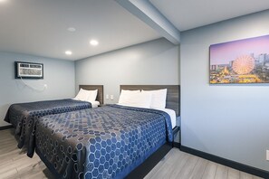 A hotel room with two beds, a cityscape painting, and a mounted air conditioner. - Hillsboro Inn & Suites (Hillsboro)