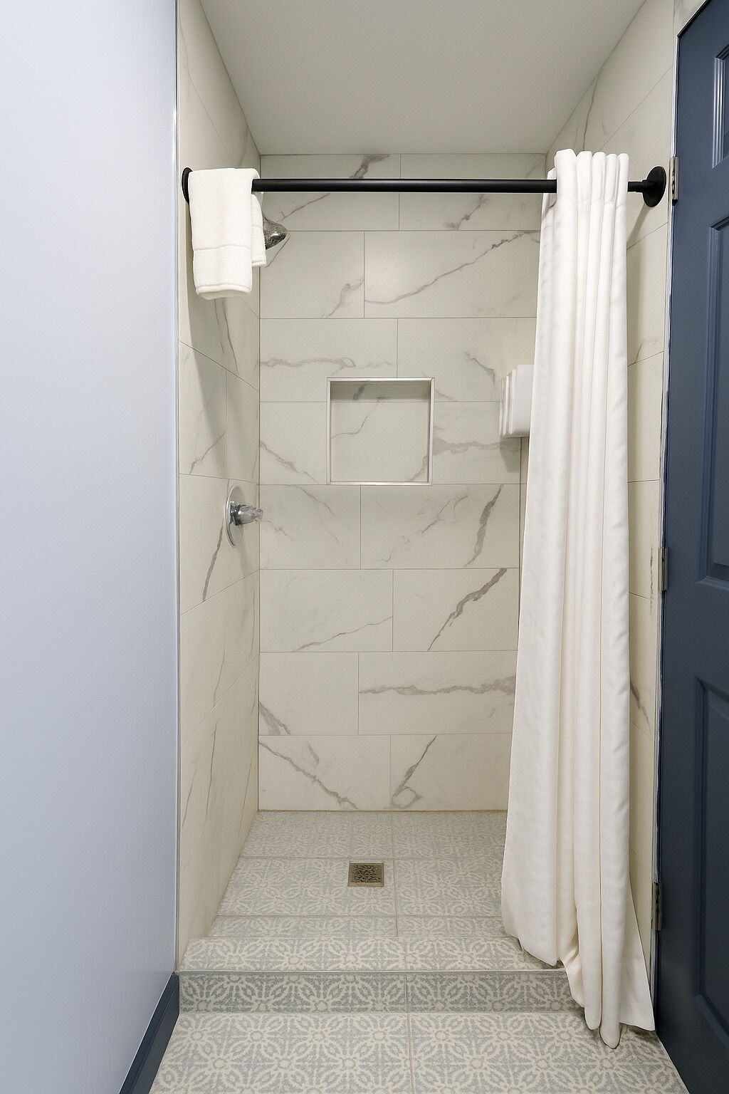 A shower area with marble walls, a showerhead, and a towel rack.