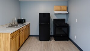 A compact kitchen with a sink, microwave, black refrigerator, stove, and wooden cabinets. - Hillsboro Inn & Suites (Hillsboro)