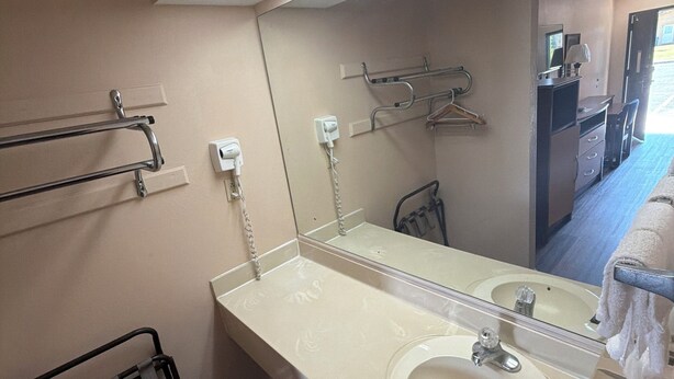 Un baño de hotel con un espejo grande, un lavamanos, un perchero para toallas y una zona de ducha.