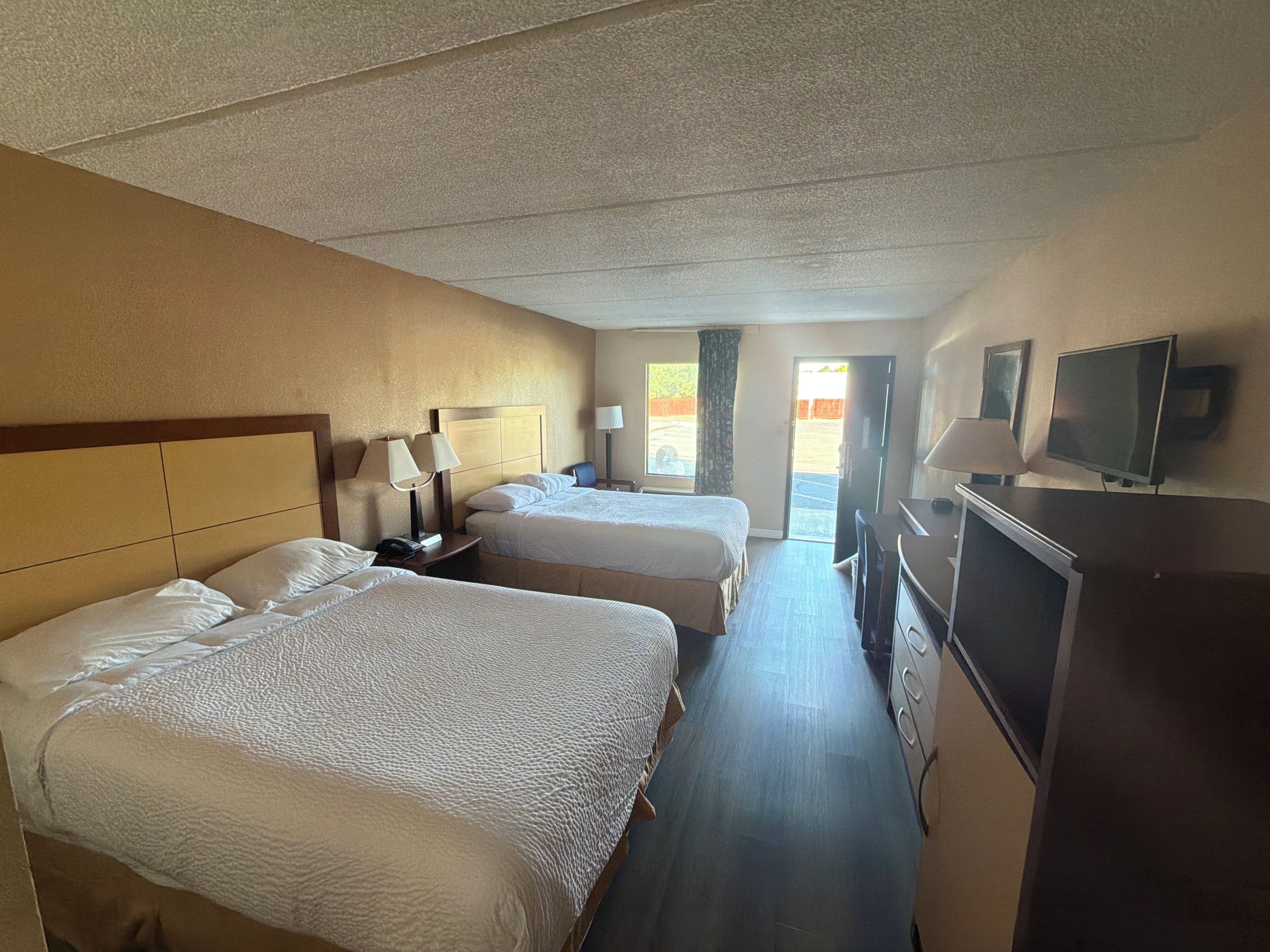 A hotel room with two beds, a desk, a TV, and a window with a view.