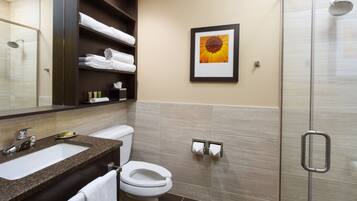 A modern bathroom with a sink, toilet, and shower. There are shelves with towels and a framed picture on the wall.