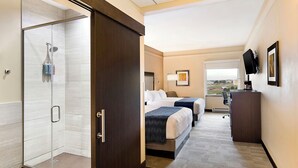 Quarto de hotel com chuveiro, duas camas, uma mesa de trabalho e vista para o exterior.