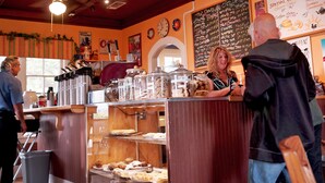 A bakery counter with various baked goods and a chalkboard menu listing items like hot drinks and cold drinks. - Fiddler's Inn (Carlsbad)