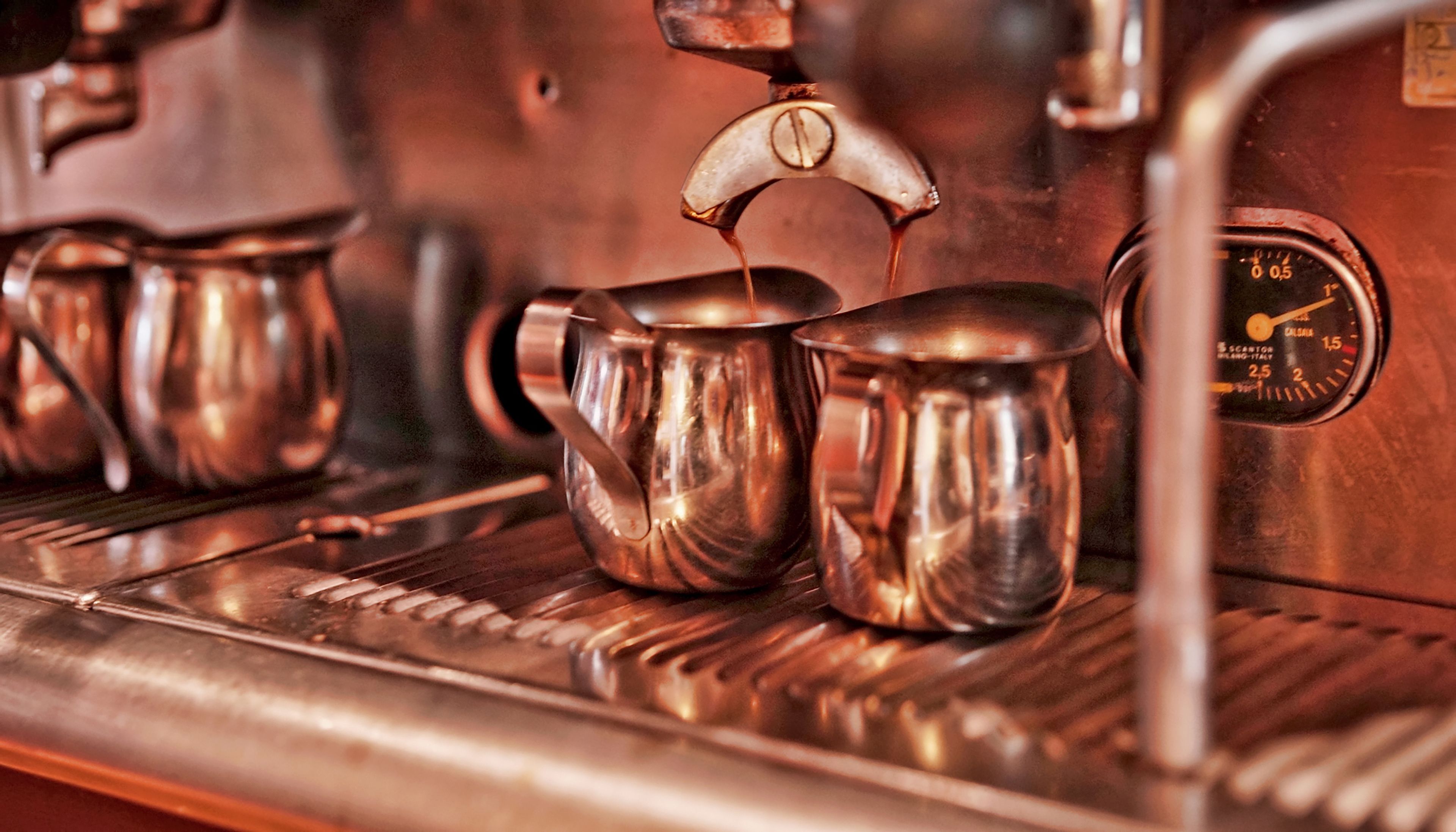 Primeiro plano de uma máquina de café a verter líquido para uma chávena de metal.