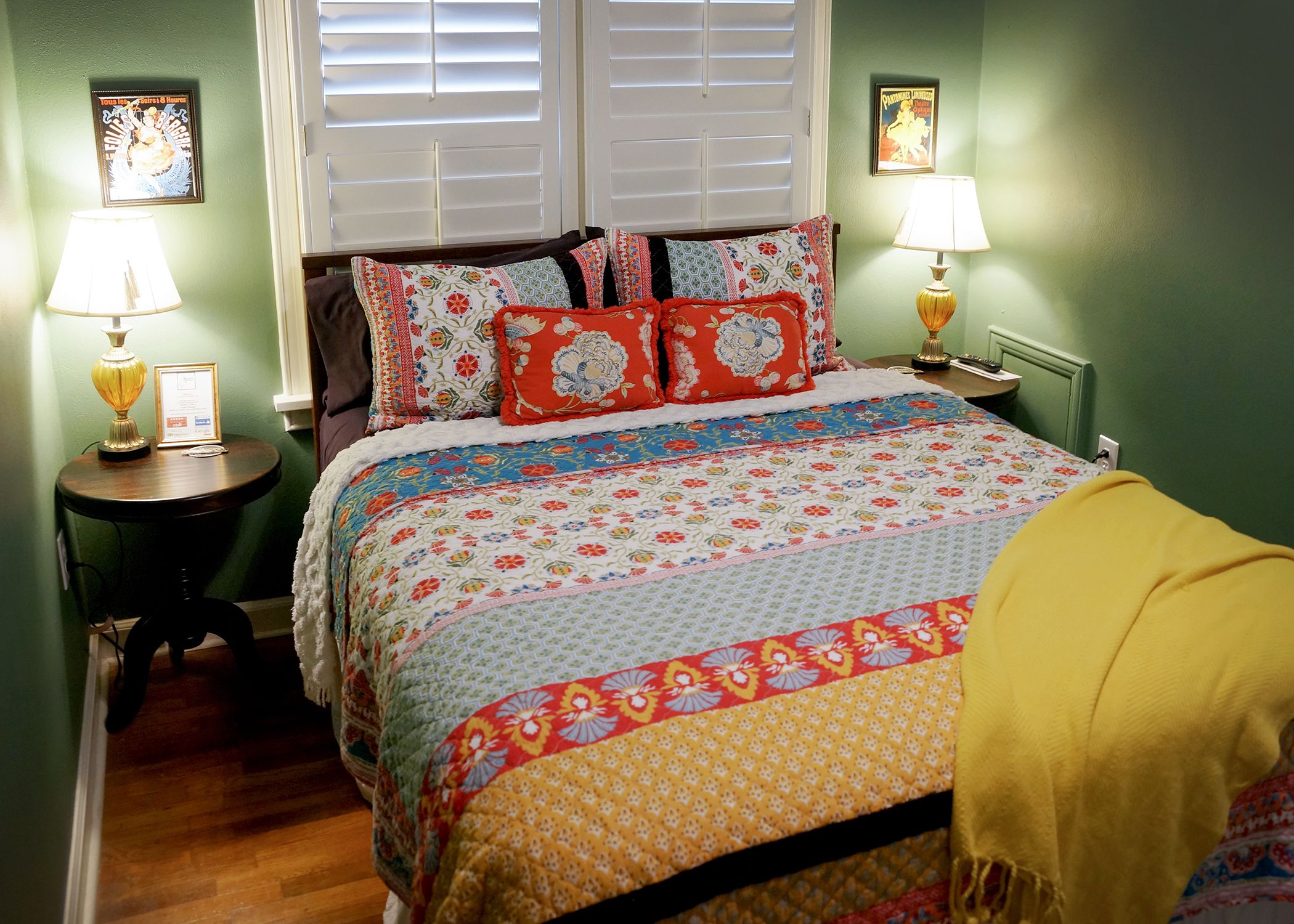 A bedroom with a bed, two bedside tables, two lamps, and a window with blinds.