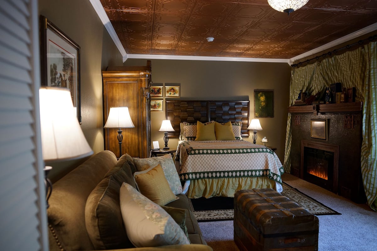 A cozy room with a bed, a wooden chest, and a fireplace.