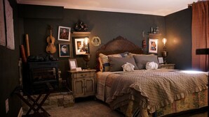 A cozy bedroom with a wooden bed, a fireplace, and various framed pictures and decorations on the walls. - Fiddler's Inn (Carlsbad)