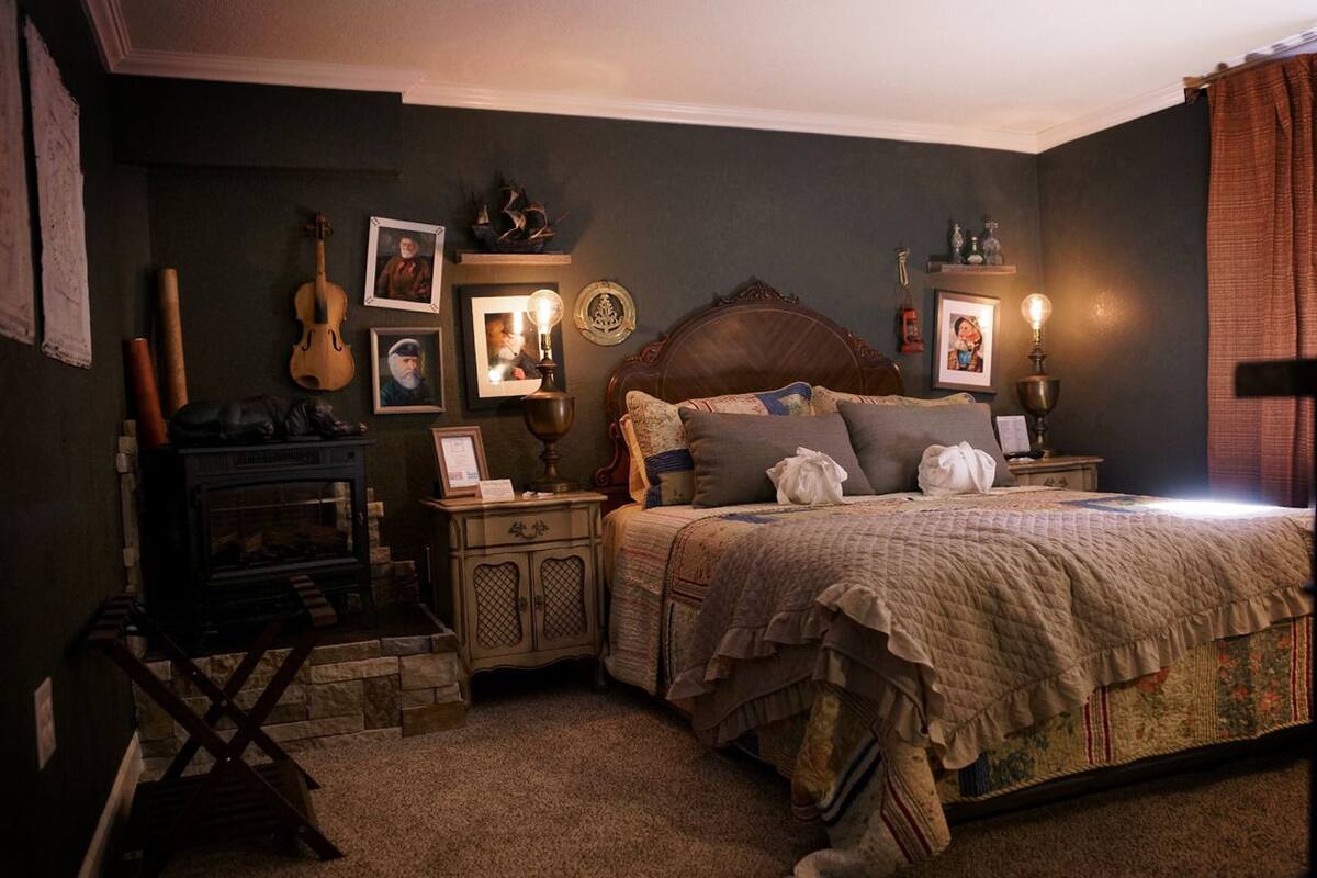 A cozy bedroom with a wooden bed, a fireplace, and various framed pictures and decorations on the walls.