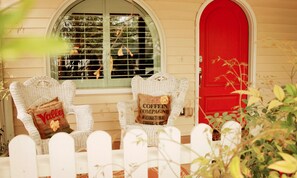 A porch with two wicker chairs, each with a cushion, and a red door. - Fiddler's Inn (Carlsbad)