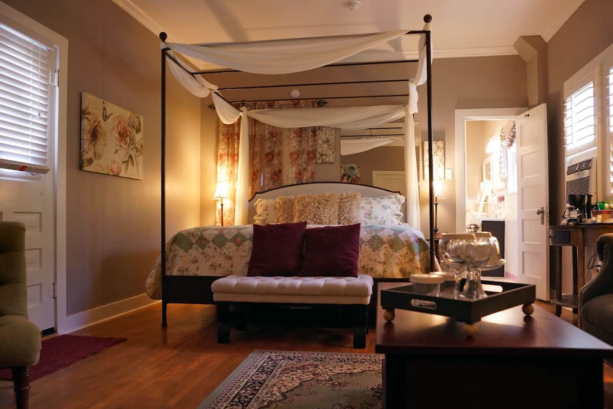 A bedroom with a four-poster bed, a bedside table with a lamp, a chair, and a rug.