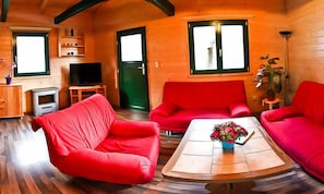 Interior acogedor de una cabaña de madera con un sofá rojo, un televisor y una mesita con un jarrón de flores.