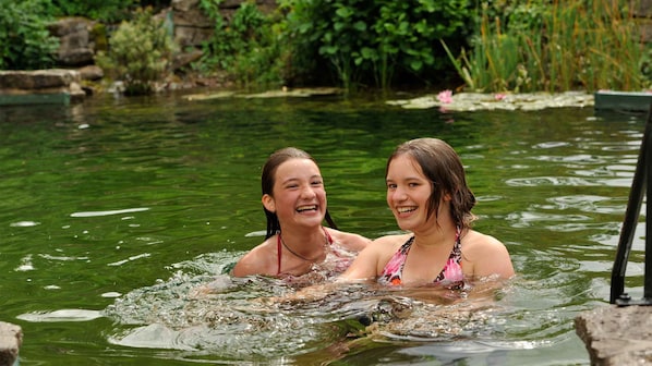 Dos personas en una masa de agua natural rodeada de vegetación.