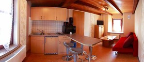 Cocina compacta con estufa integrada, un lavamanos y un pequeño comedor con un sofá rojo.