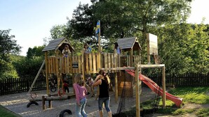 A wooden play structure with a slide and climbing elements, surrounded by a fenced area. - Landgasthof Probstei Zella (Amt Creuzburg)