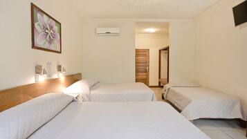A hotel room with three single beds, a wooden headboard, a wall-mounted air conditioner, and a door leading to another room.
