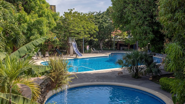 A pool area with a slide, surrounded by lush greenery and a clear blue pool. - Hotel Boyeros (Liberia)