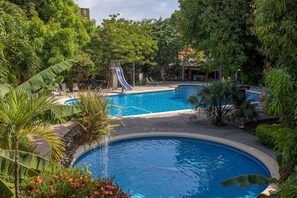 A pool area with a slide, surrounded by lush greenery and a clear blue pool. - Hotel Boyeros (Liberia)