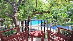 A wooden bench and table on a balcony overlooking a pool area. - Hotel Boyeros (Liberia)