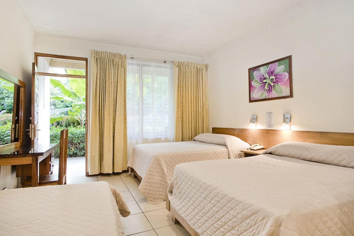 Une chambre d’hôtel avec deux lits, un bureau, une chaise et une grande fenêtre avec des rideaux.