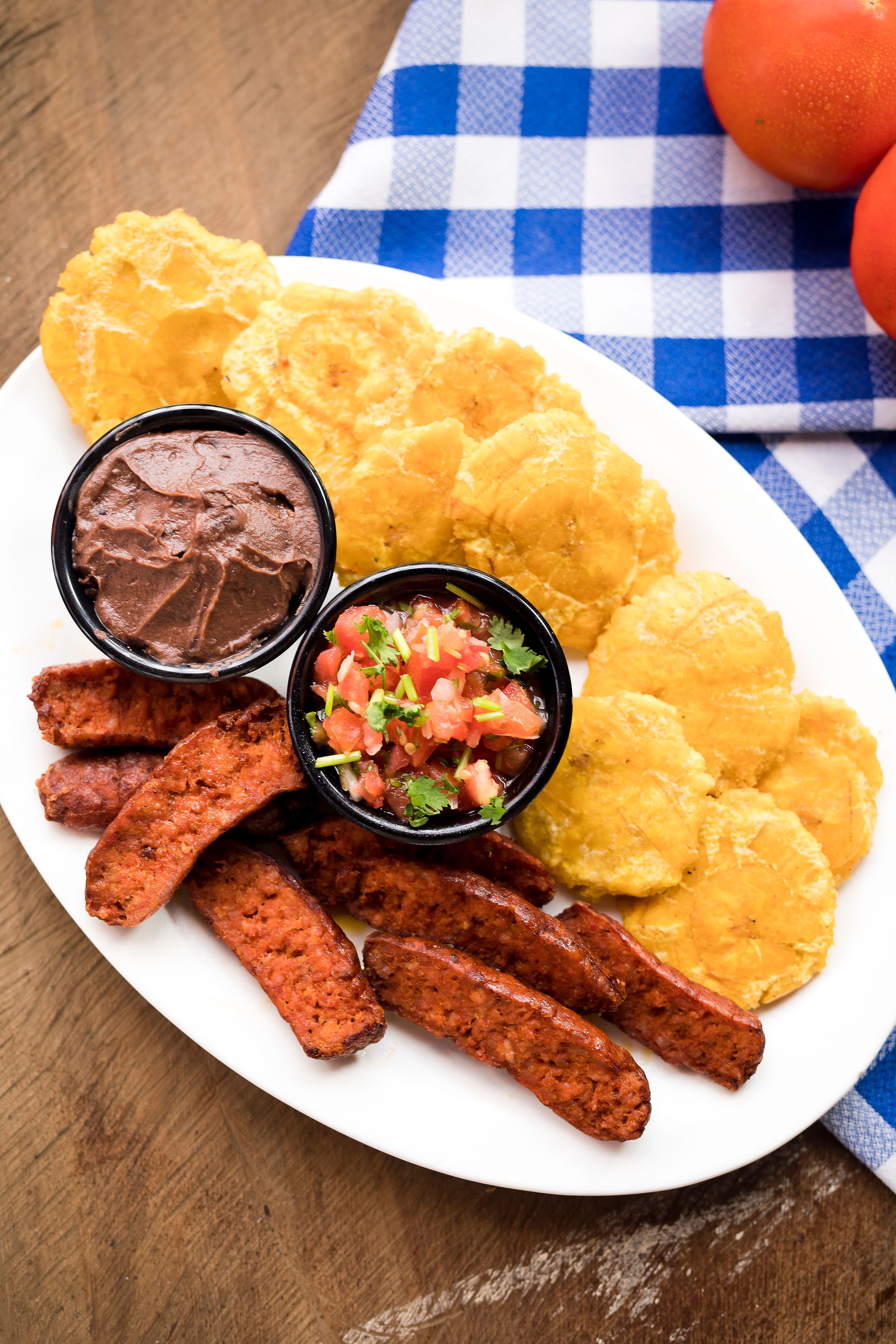 Een bord met gebakken plantains, een kom bonen, salsa en gegrild vlees.