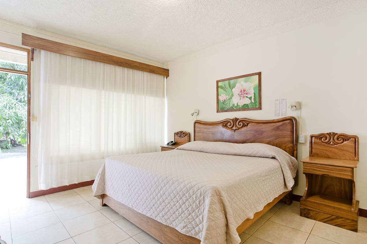 Une chambre à coucher avec un lit, une table de chevet, une lampe fixée au mur et une fenêtre avec des rideaux.