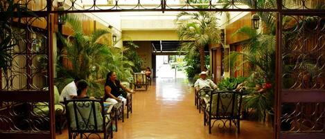 A corridor with chairs and tables, surrounded by lush green plants.