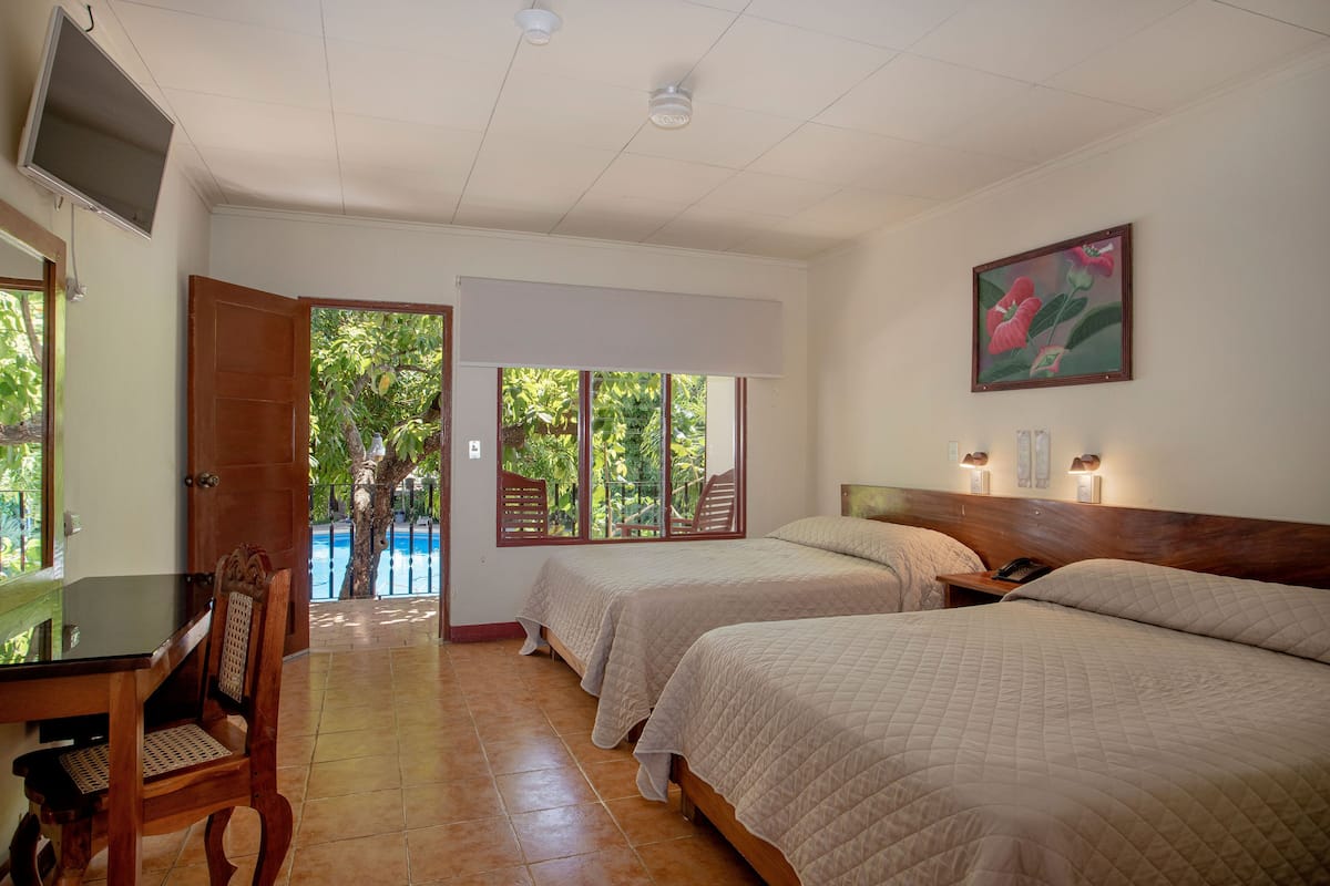 Une chambre d’hôtel avec deux lits, un bureau, une chaise, une télévision et un tableau au mur.