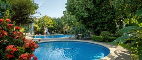 A circular pool surrounded by lush greenery and red flowers.