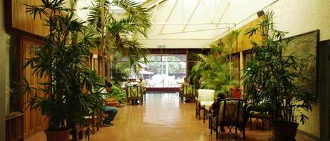 A spacious indoor corridor with wooden walls and large potted plants.