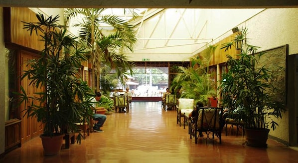 Un vaste couloir intérieur aux murs en bois et agrémenté de grandes plantes en pot.