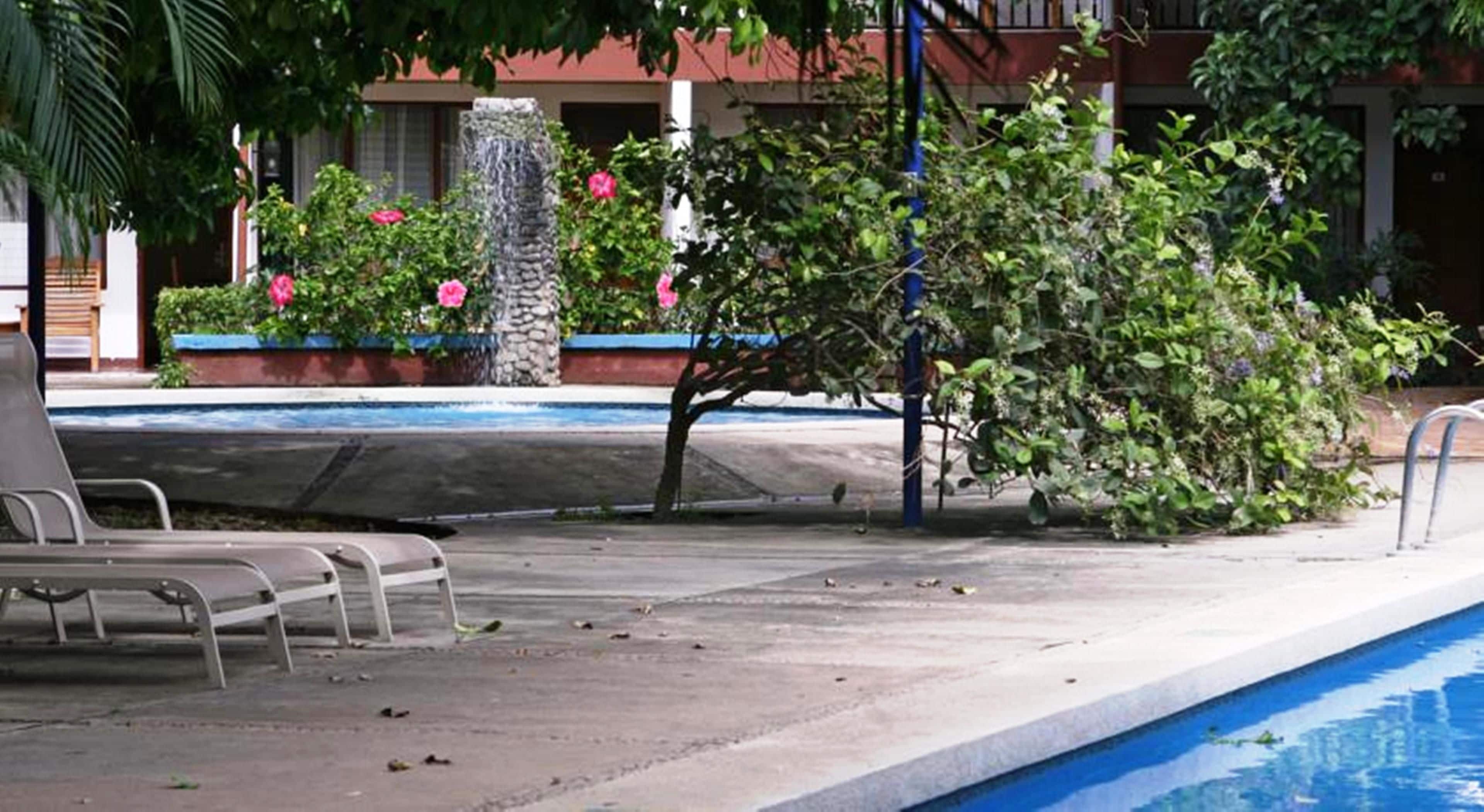 Ein Poolbereich mit Liegestühlen, einer Steinsäule und einem Gebäude im Hintergrund.
