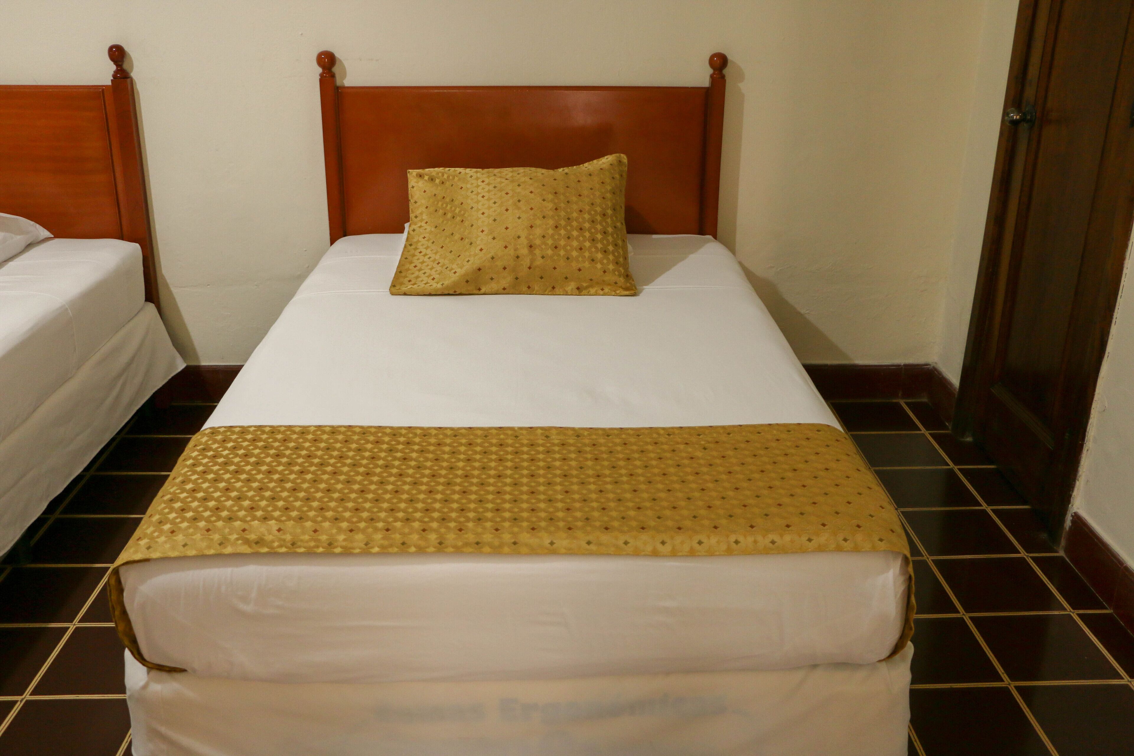 A single bed with a wooden headboard, a patterned pillow, and a beige bedspread.