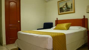 A hotel room with a bed, a chair, a door, and a painting on the wall.