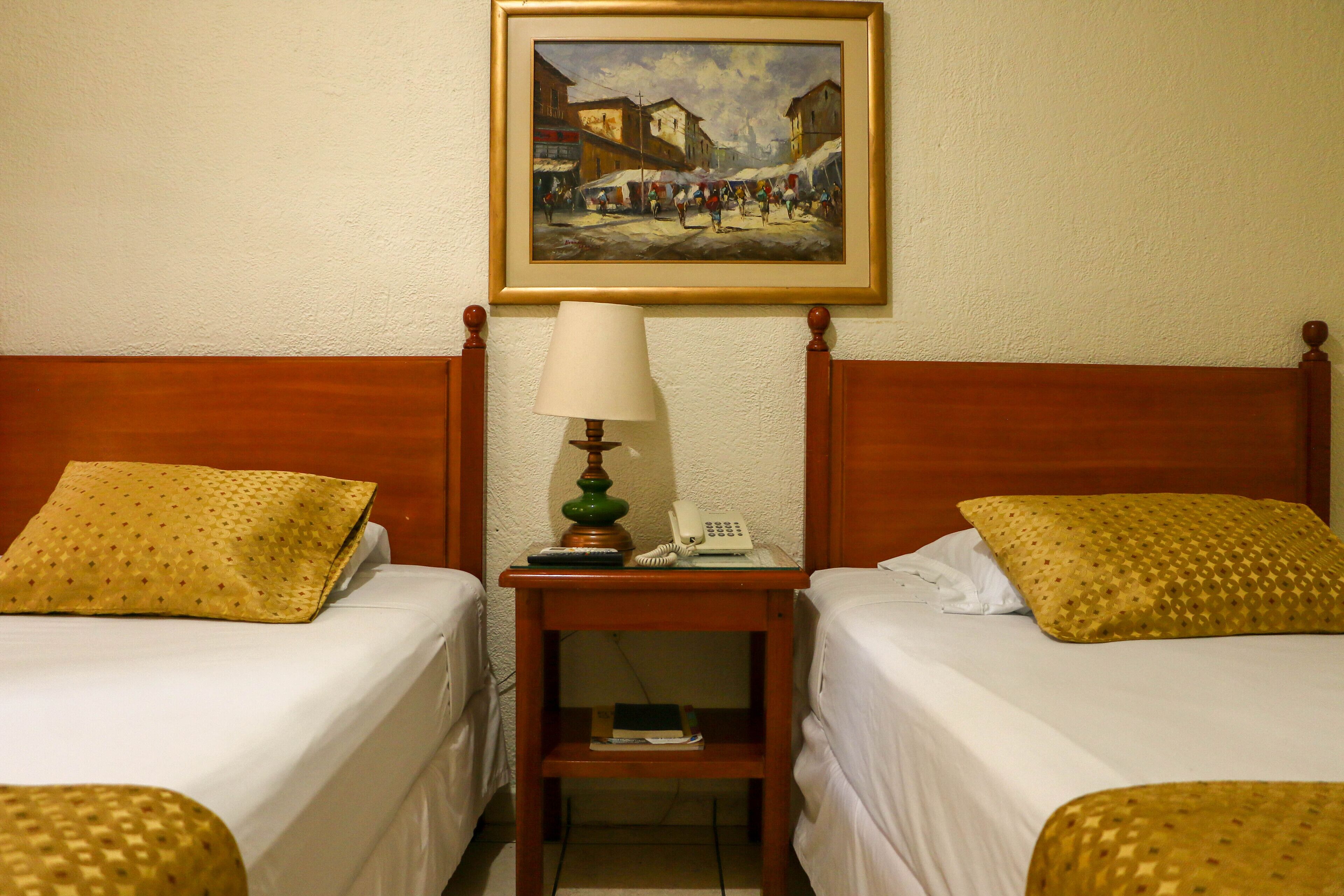 Une chambre d’hôtel avec deux lits, une table de chevet avec une lampe, un téléphone et un tableau au mur.