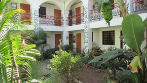 Um edifício com vários andares e um pátio central, rodeado por vegetação exuberante e diversas plantas.