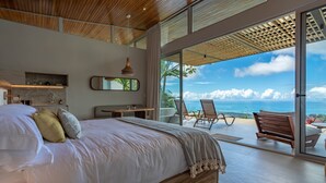 Une chambre moderne avec un grand lit, un plafond en bois, une vue sur l’océan et un balcon aménagé avec des sièges.