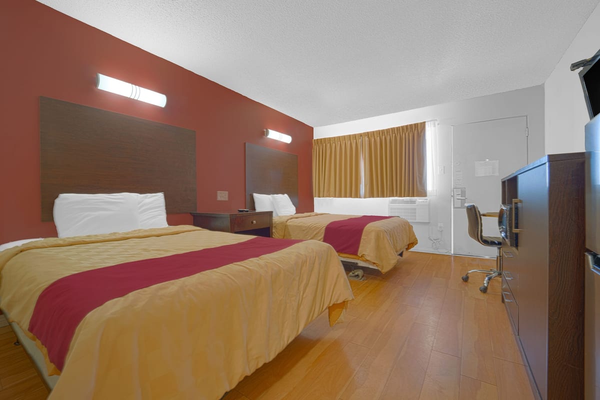 Una habitación de hotel con dos camas, un escritorio, una silla, un televisor y una ventana con cortinas.