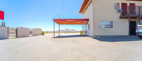 A gas station with a clear sky, a red canopy, and a building with a balcony.