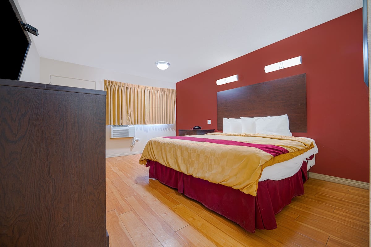 Una habitación de hotel con una cama grande, suelo de madera, una pared de acento roja e iluminación en el techo.