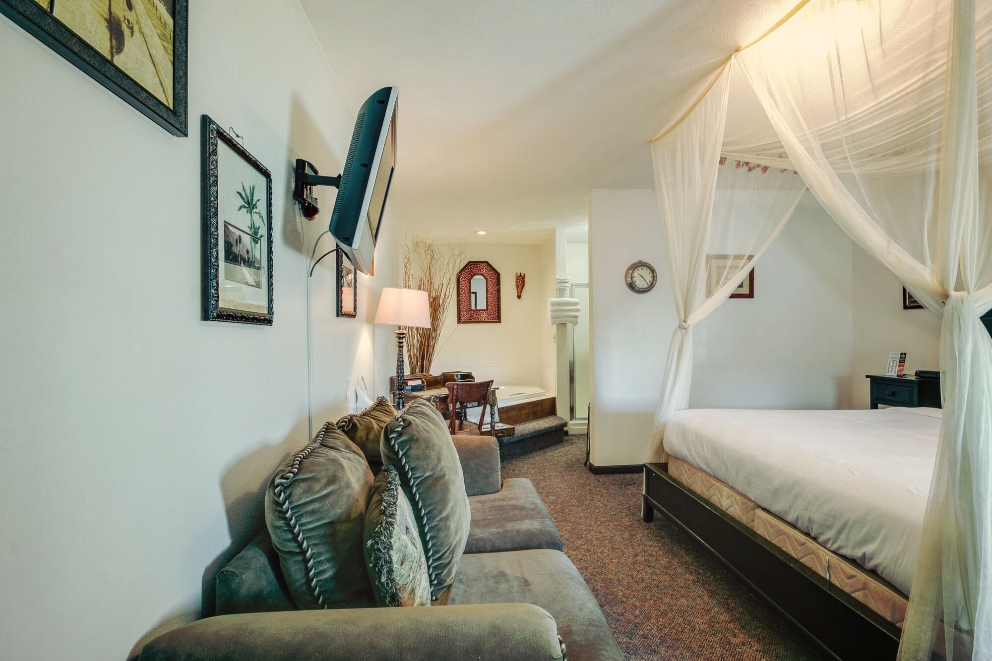A bedroom with a bed, a sofa, a lamp, and a mirror.