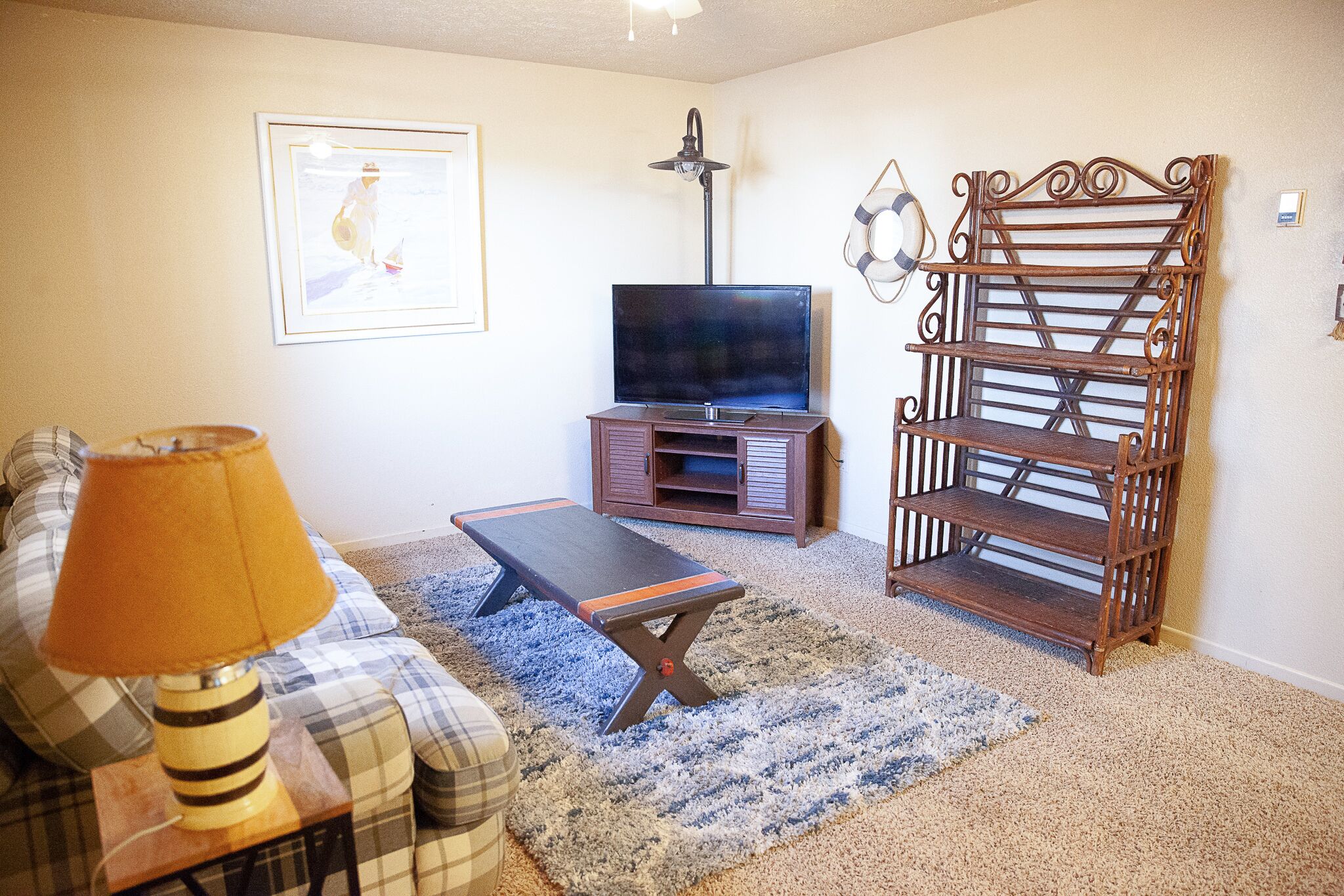 A living room with a television, a bench, a lamp, a sofa, and a wooden shelf.