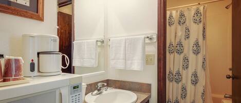 A bathroom with a sink, a coffee maker, and a shower curtain.